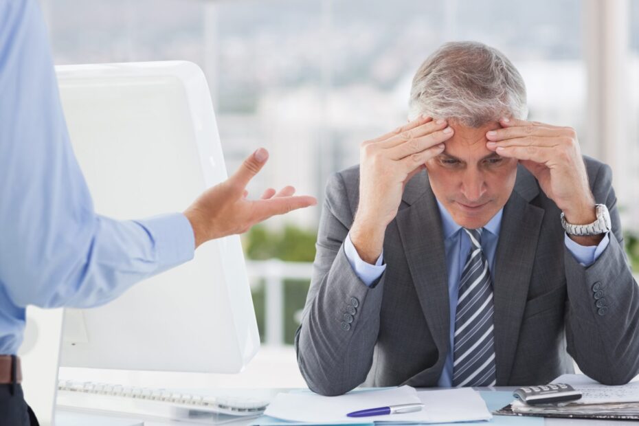 An image of an employee holding his head in disappointment while receiving bad feedback from an employeer