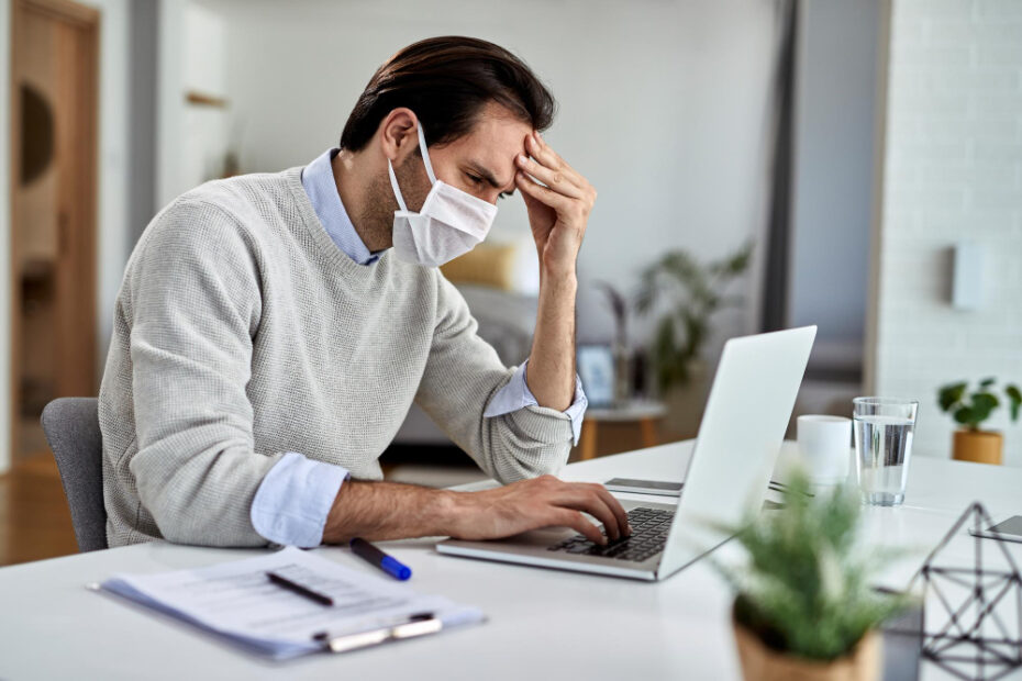 Worried freelance worker wearing protective face mask while reading problematic email computer working home during virus epidemic.