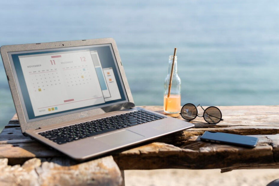 An image of a laptop and a sunglasses pair and bottle of orange juice at the beach.