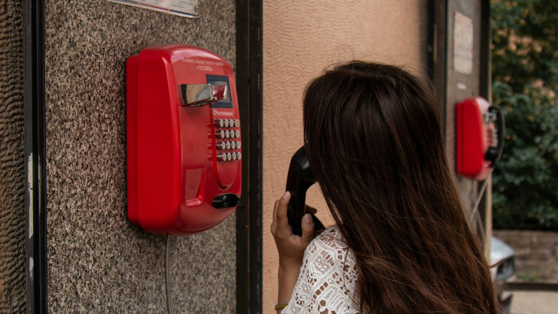An image of a female employee talking on a public telephone hanged on the wall in the middle of the street.