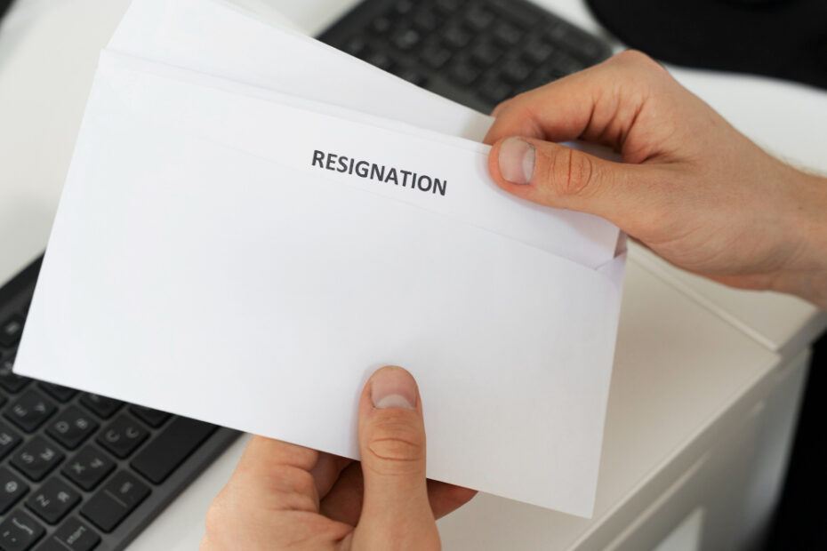 An image shows a hand holding a resignation letter in the office