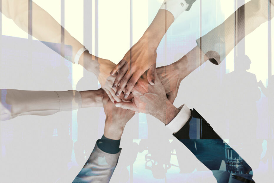 Five employees celebrating teamwork by placing their hands together in the center, symbolizing unity and collaboration.