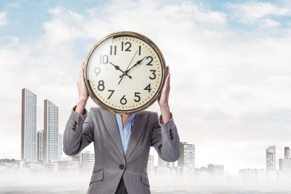 A person in a business suit stands against a cityscape background, holding a large clock in front of their face, symbolizing the concept of time management and the importance of tracking time effectively.