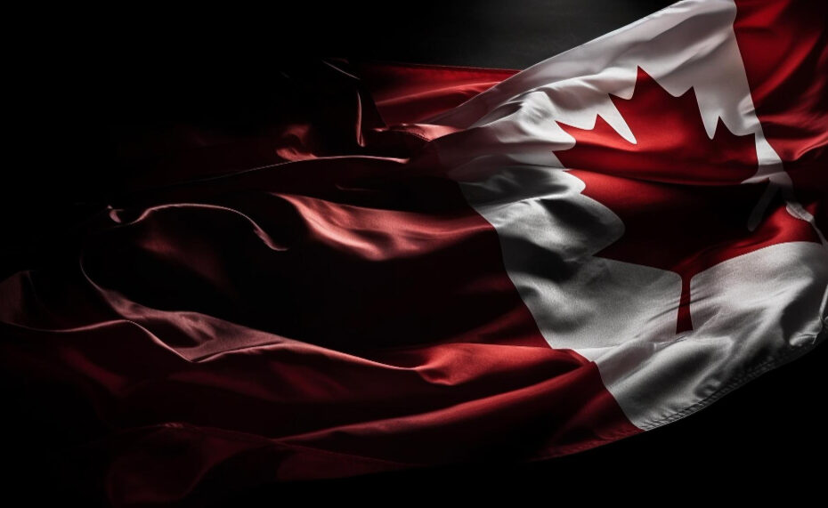 A close-up of the Canadian flag, partially illuminated against a dark background. The flag's fabric appears textured and wavy, with the red maple leaf prominently displayed. The lighting highlights the rich red and white colors, giving the flag a dramatic and reverent appearance.
