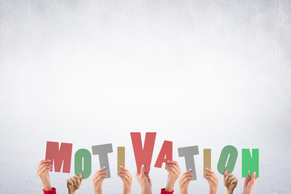 Hands holding up colorful cutout letters against a grey background that spell out the word "MOTIVATION".