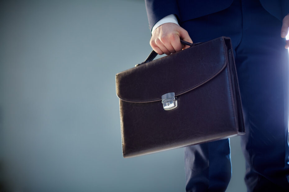 A close-up of a professional holding a leather briefcase, symbolizing the role and responsibilities of a direct employee in a corporate setting.