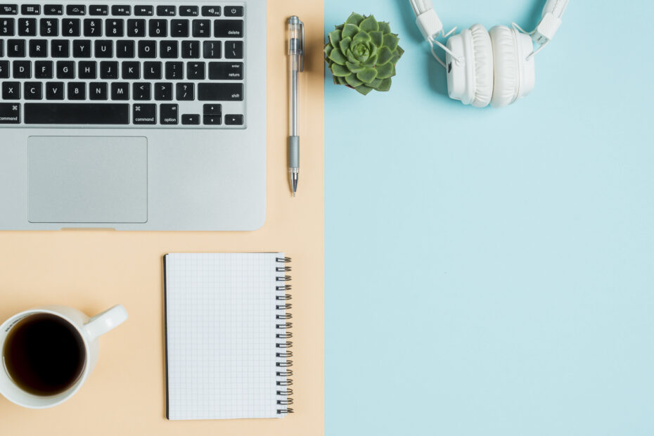 A workspace featuring remote work tools, including a laptop, pen, notebook, coffee cup, headphones, and a succulent plant, arranged on a split pastel background of peach and blue, representing productivity and balance.