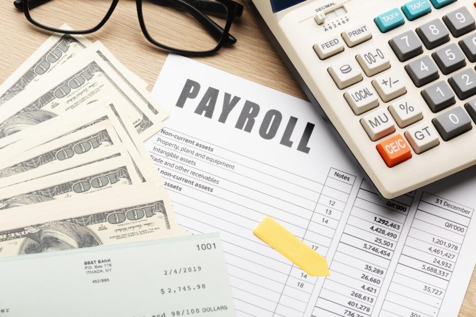 A desk setup with cash, a payroll document, calculator, and check representing the financial and administrative aspects of managing international payroll efficiently.