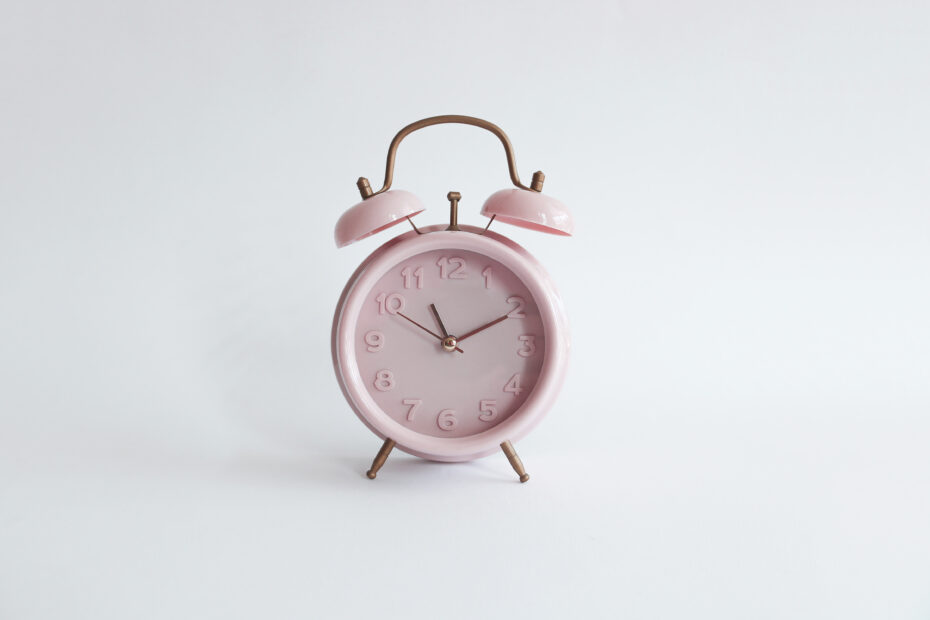 A pastel pink vintage alarm clock with bronze accents, set against a minimalistic white background, representing the concept of PTO rollover and the importance of managing unused time off before it expires.