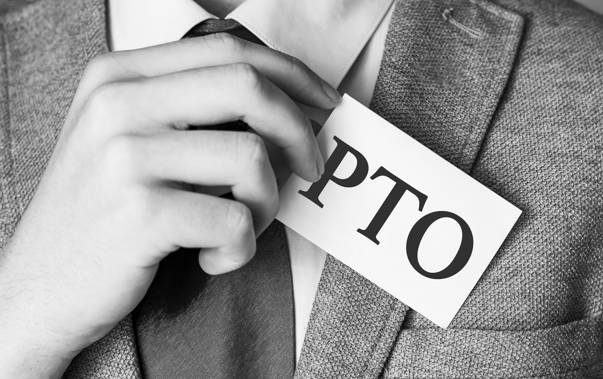 A black-and-white image of a professional in a suit holding a card with "PTO" written on it, symbolizing the concept of how PTO accrues in the workplace.