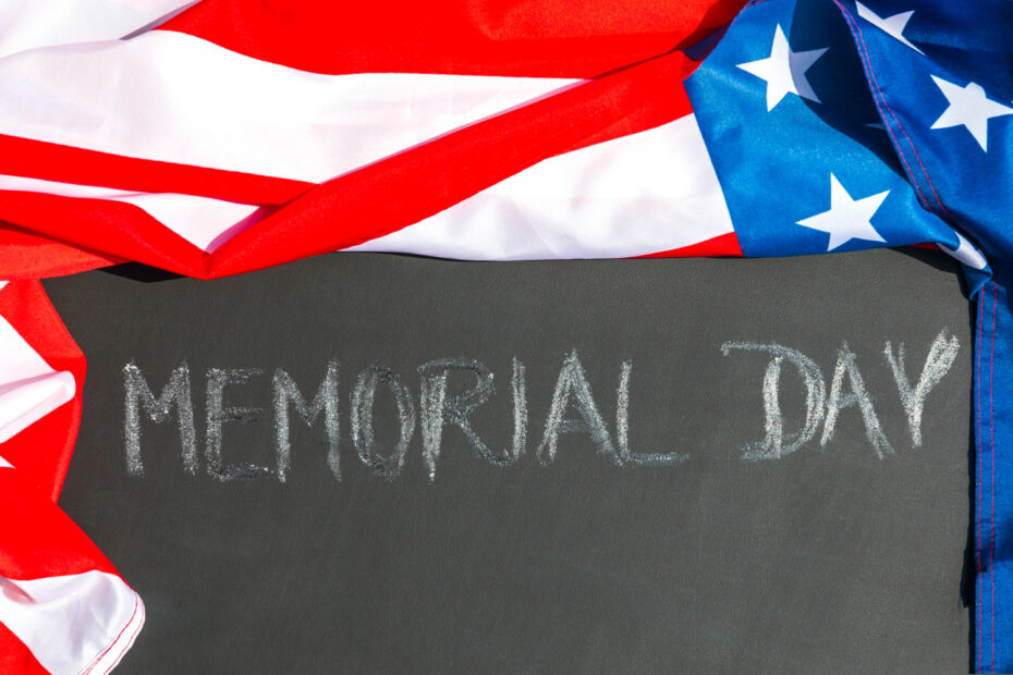 A chalkboard with "Memorial Day" written in white chalk, partially covered by an American flag. This image symbolizes remembrance and tribute for Memorial Day 2025.