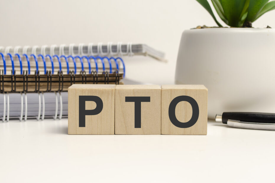 Wooden blocks spelling 'PTO' placed on a desk with office supplies, symbolizing PTO payout policies and workplace benefits.