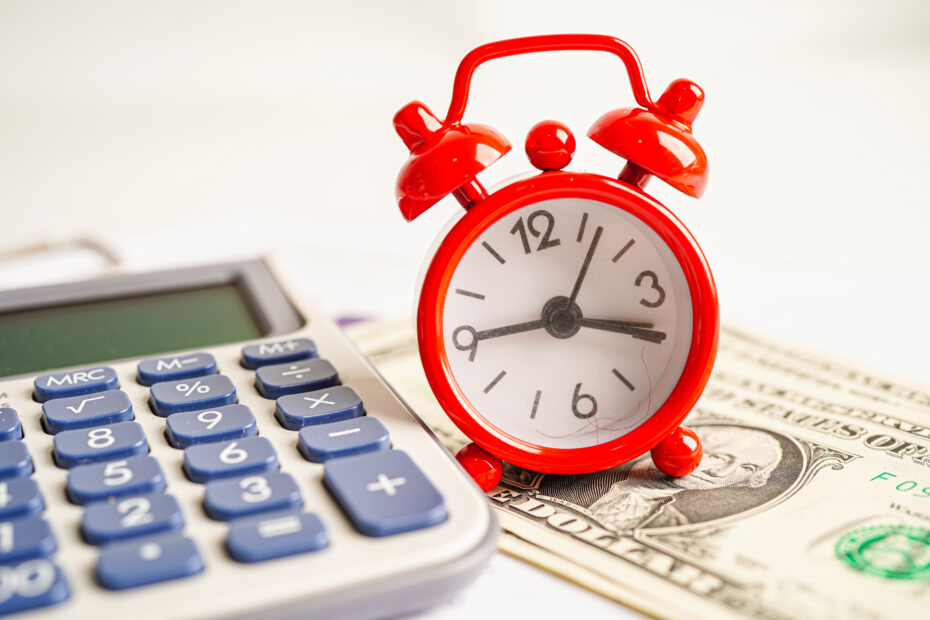 A red alarm clock placed on a U.S. dollar bill next to a calculator, symbolizing the concept of Time Off in Lieu (TOIL) and the balance between extra work hours and financial compensation.