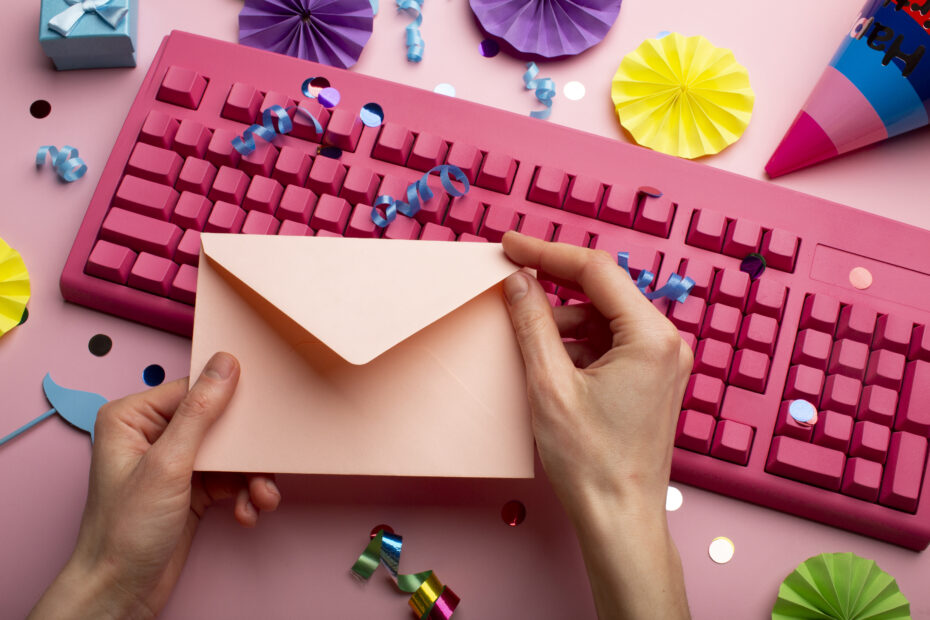 Hands holding a pastel pink envelope over a vibrant pink keyboard, surrounded by colorful confetti and decorations, symbolizing a festive approach to sending a planned leave mail.